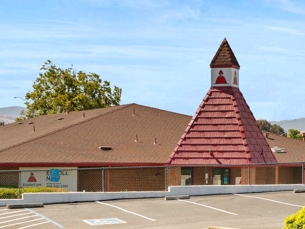Childcare building with a red pointed roof and bell tower, asphalt parking lot