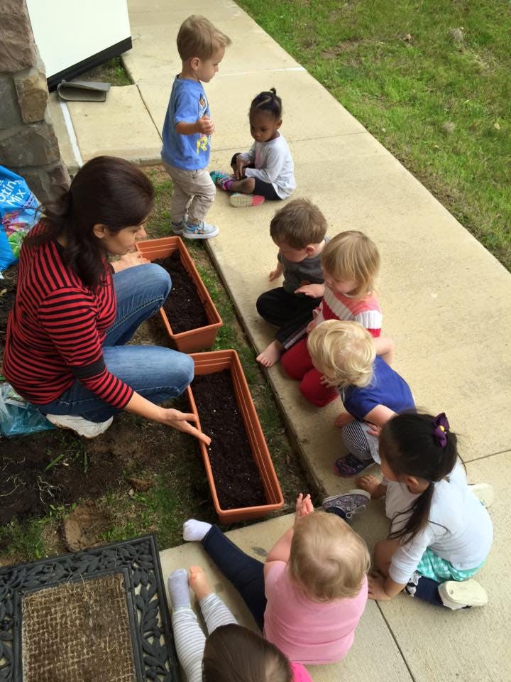 Adult and multiple children gathered around planters with soil