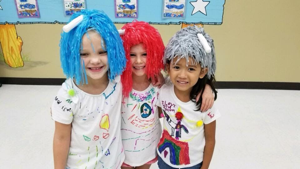 Three children wearing colorful wigs and decorated shirts