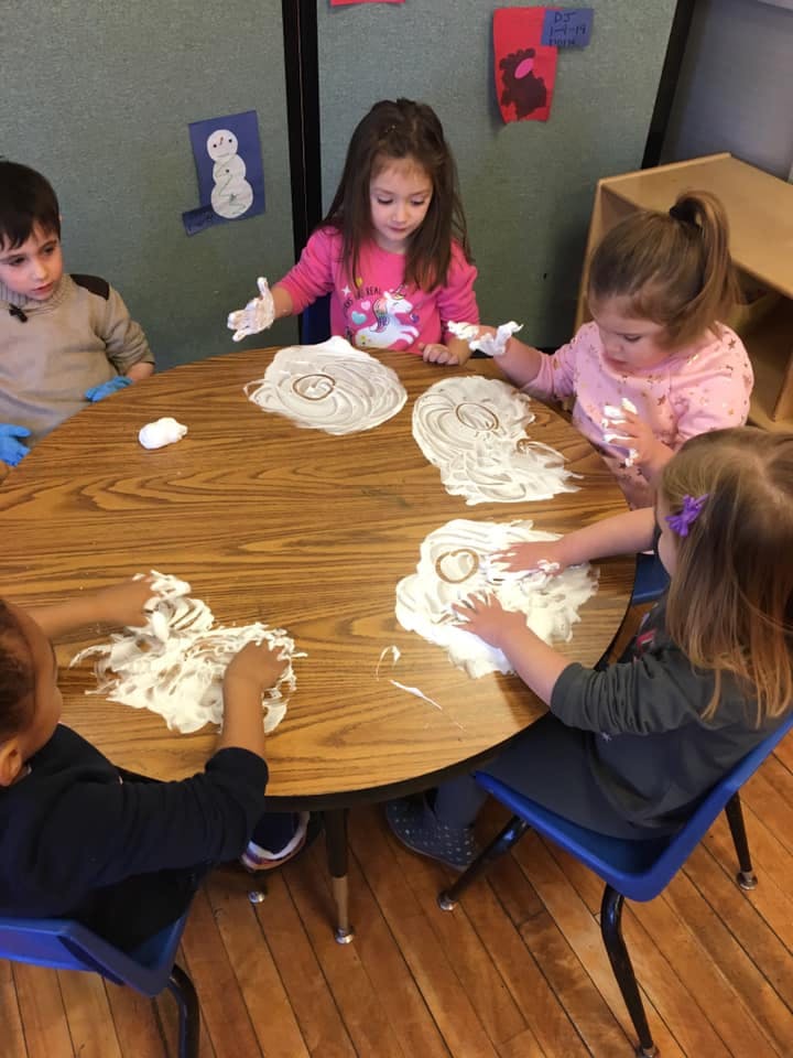 Children playing with shaving cream on a table in a classroom