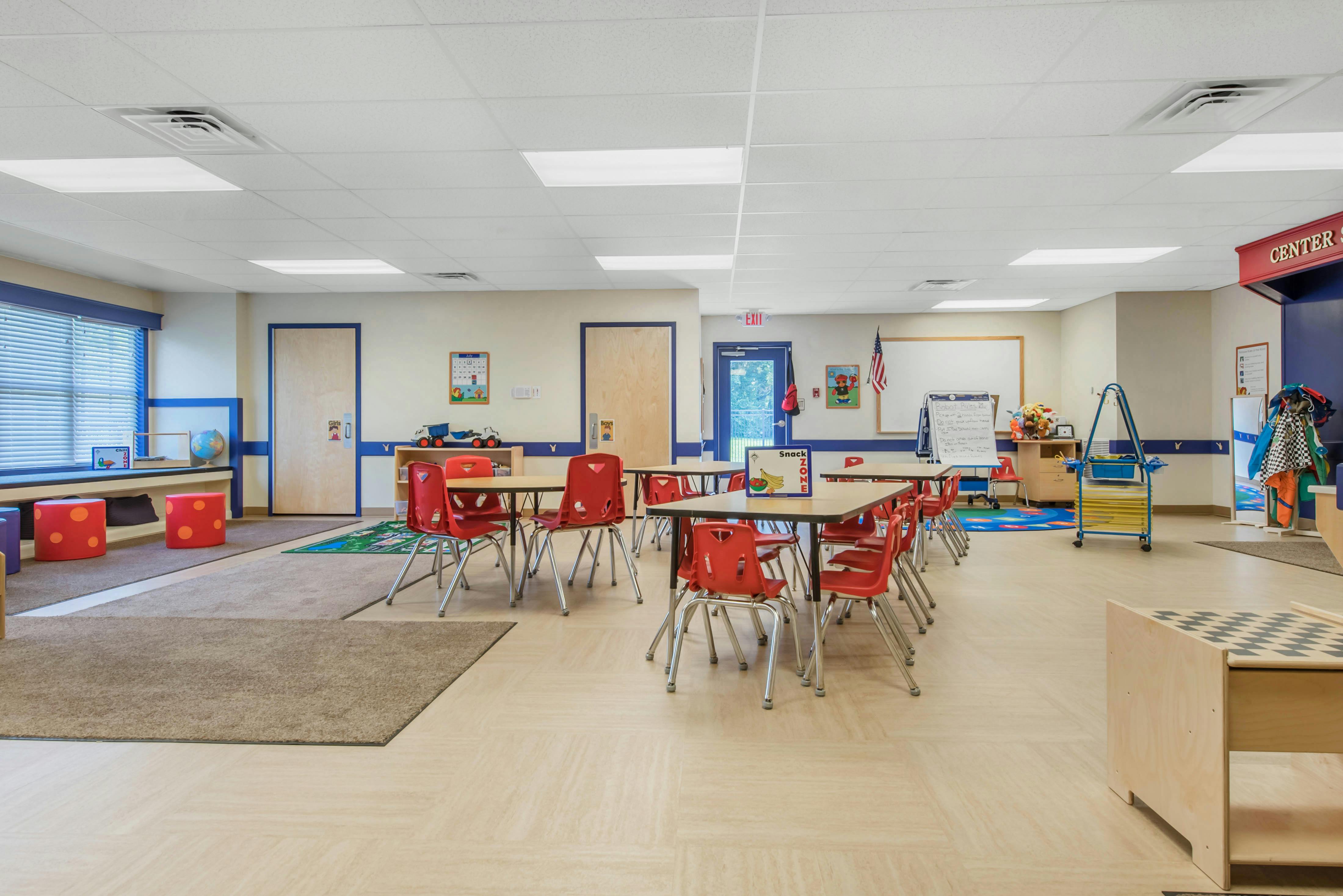 Classroom with small tables and red chairs, window seat, and learning areas