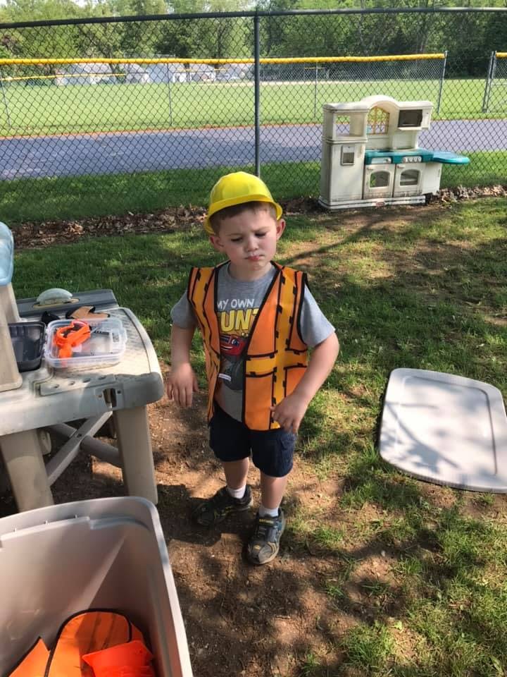 Child in a yellow hard hat and orange safety vest standing outdoors