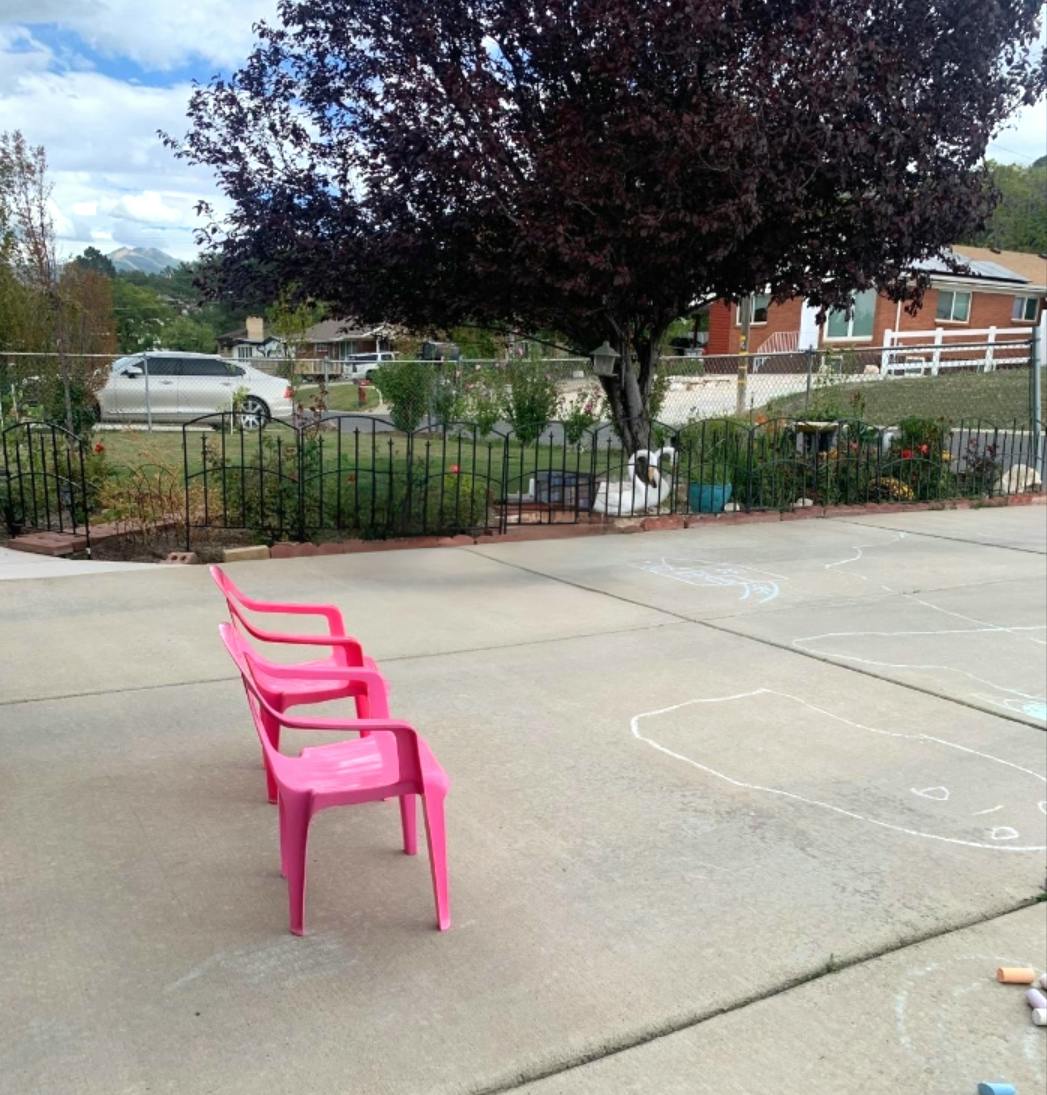 Three pink chairs in a row on a concrete driveway with chalk drawings