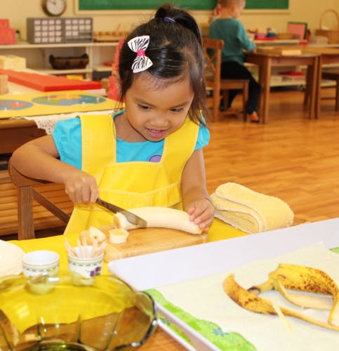 Child in yellow apron cutting a banana on a wooden board