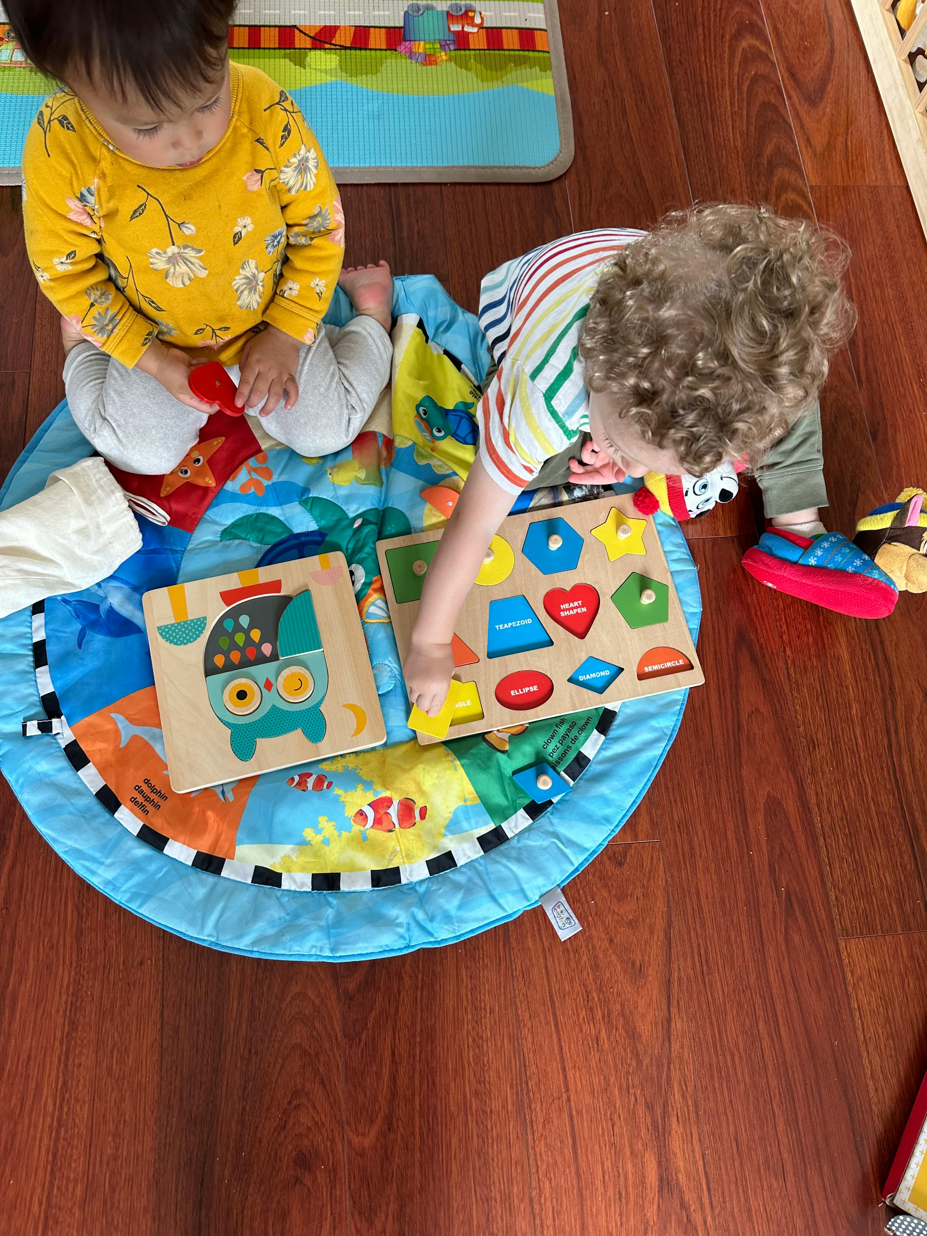 Two children playing with shape sorter puzzles on a mat