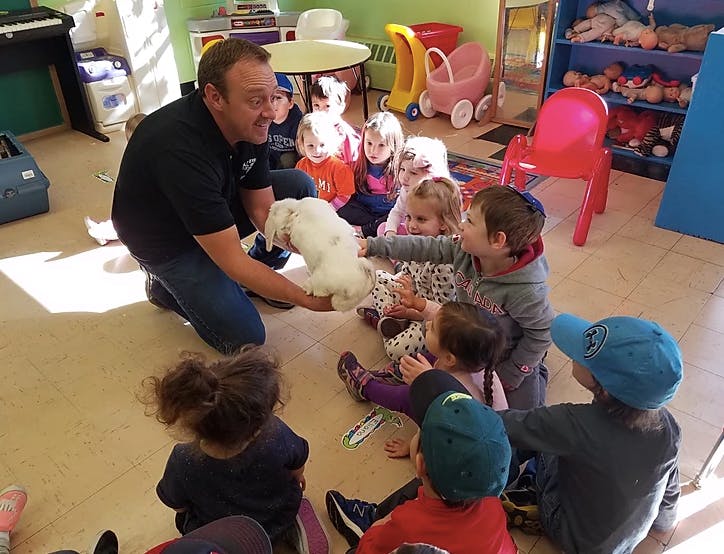 Person kneeling and holding a white rabbit for a group of children
