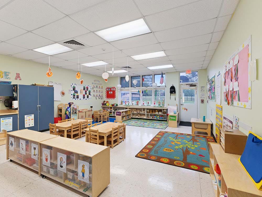 Classroom with small wooden tables and chairs, and a colorful rug