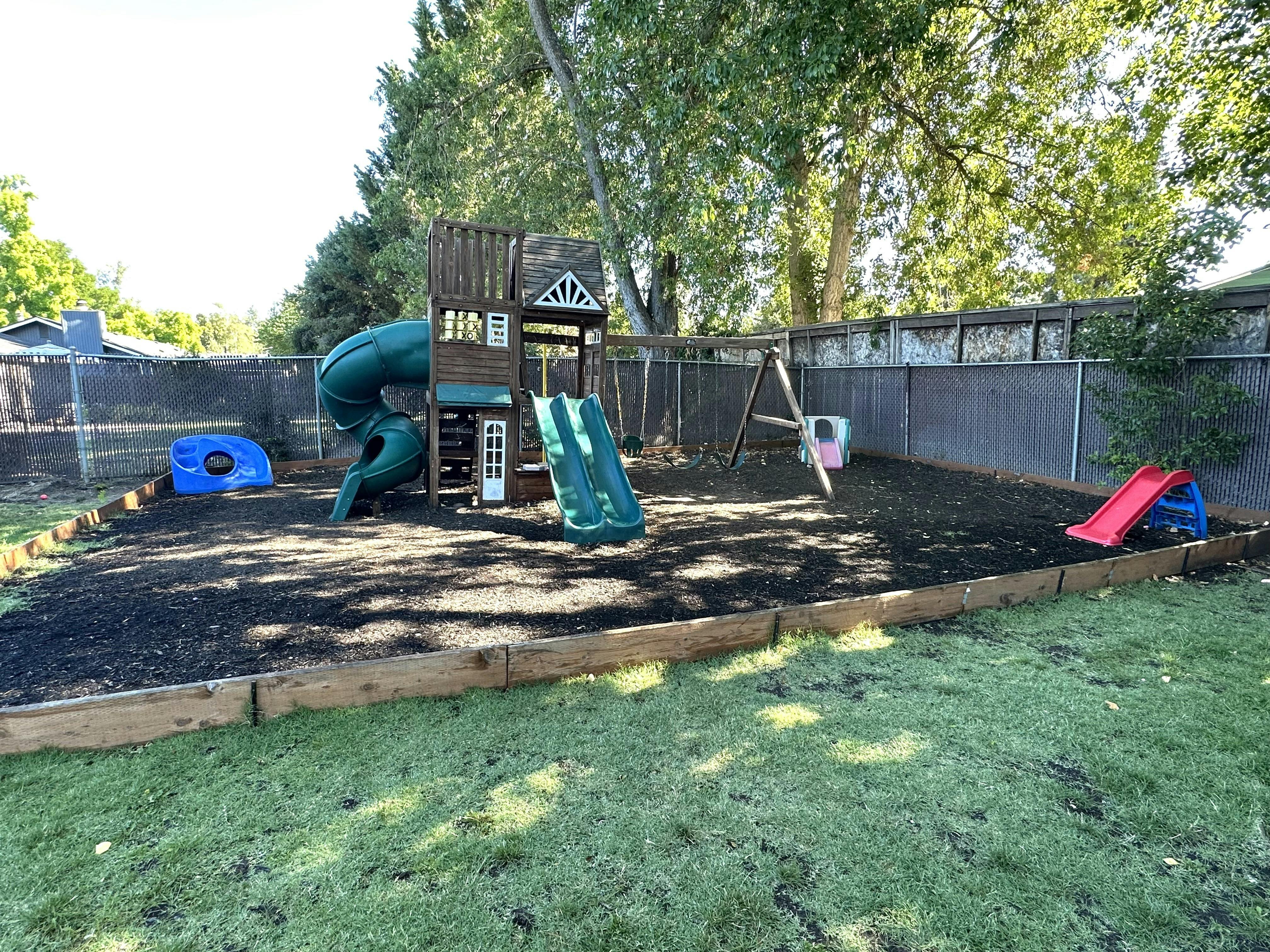 Wooden playground structure with slides and swings in a fenced backyard