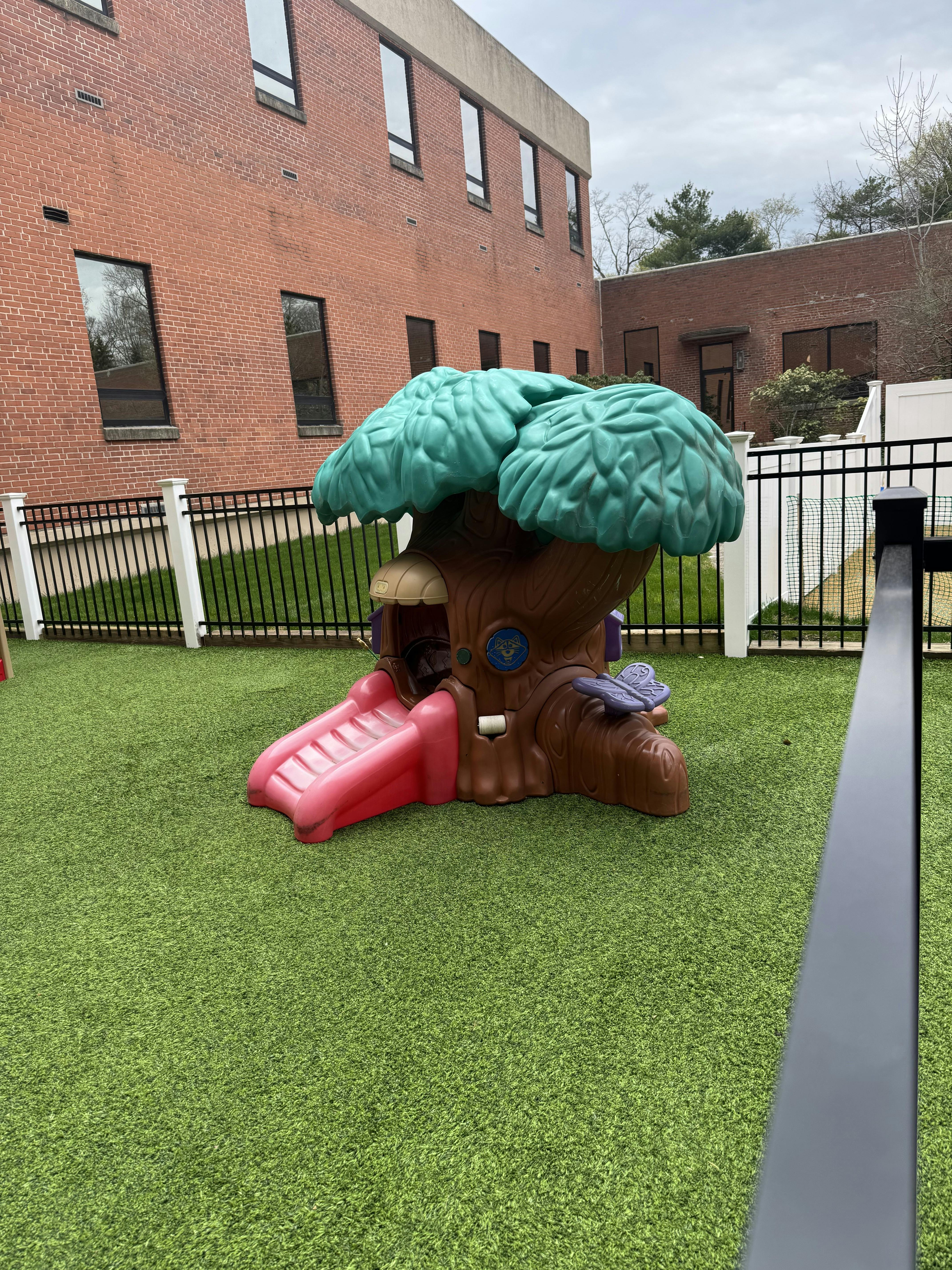 Plastic treehouse play structure with a pink slide on artificial grass