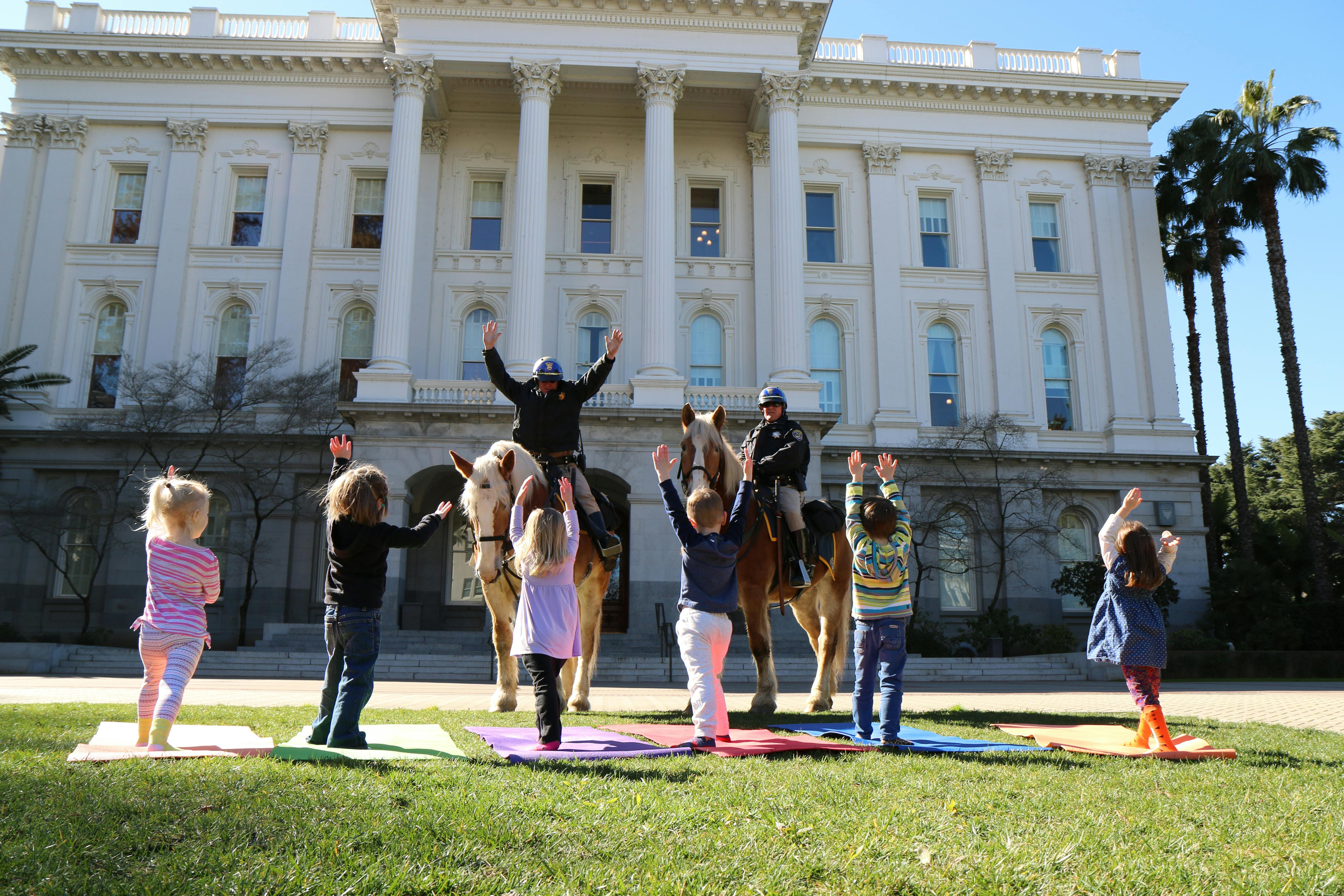 People on horses and children on yoga mats in front of a large building