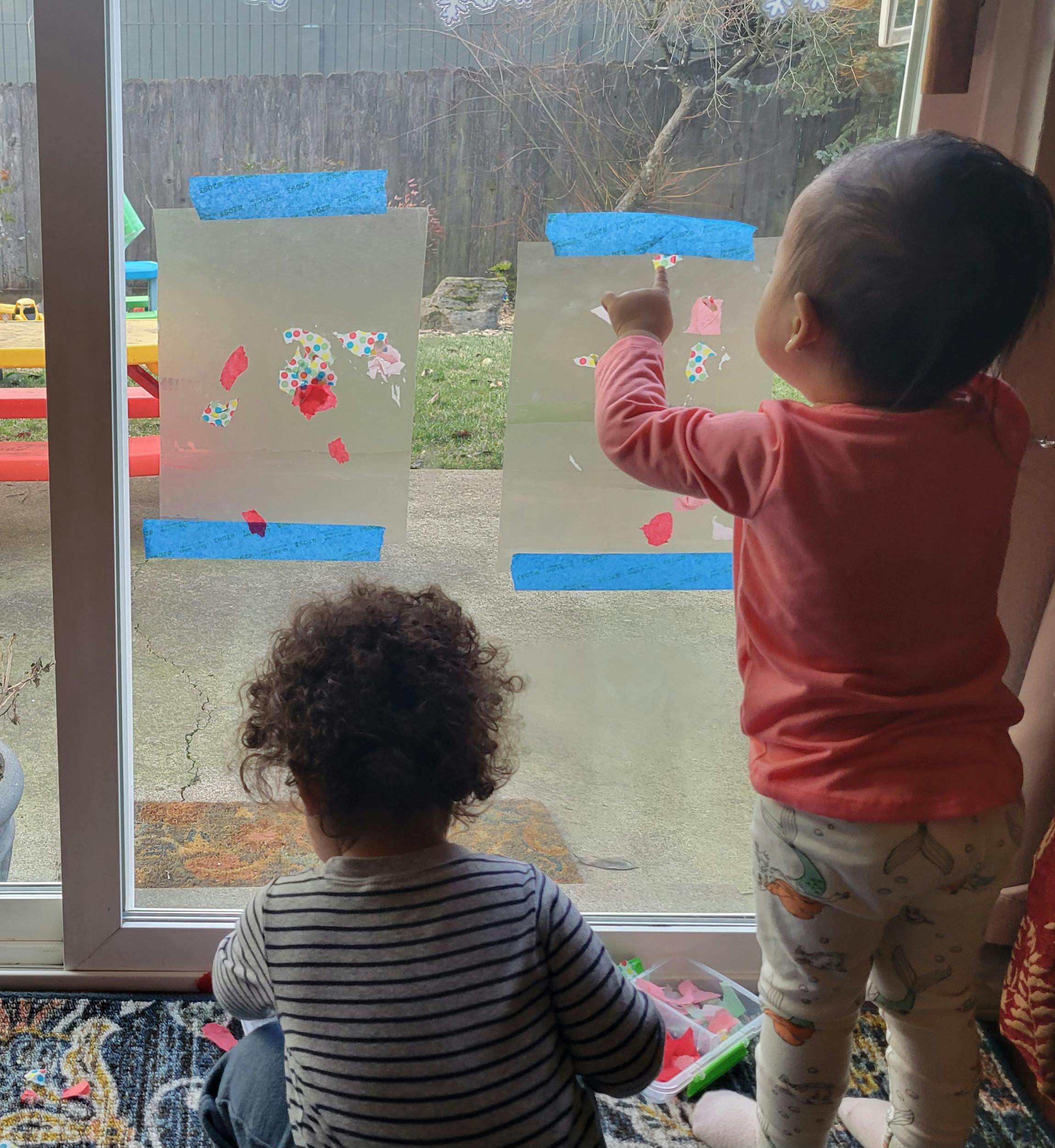 Two children playing with art supplies on a glass door