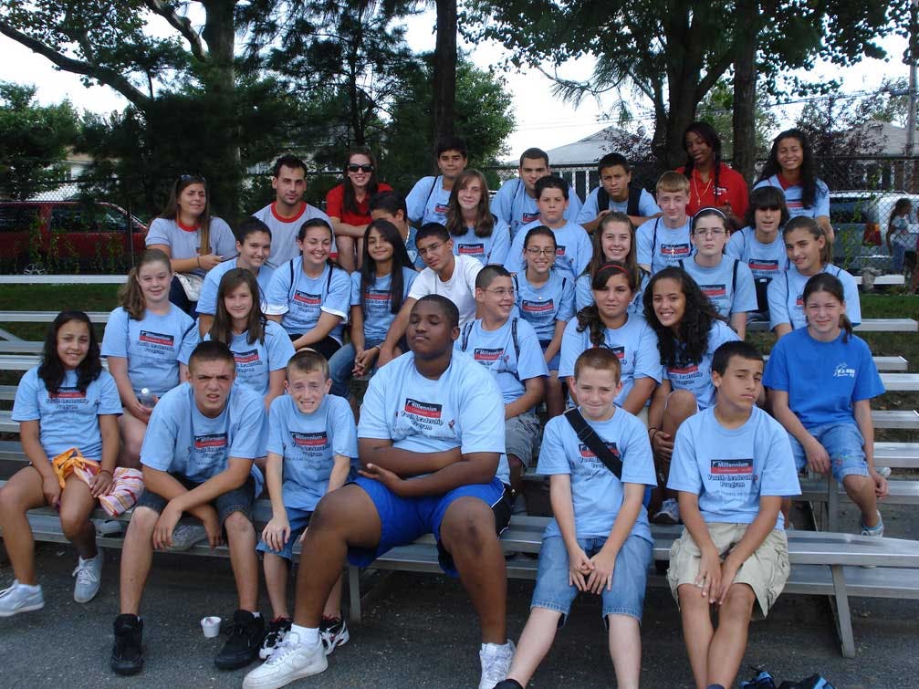 Group of people and teens in light blue shirts sitting on bleachers outdoors