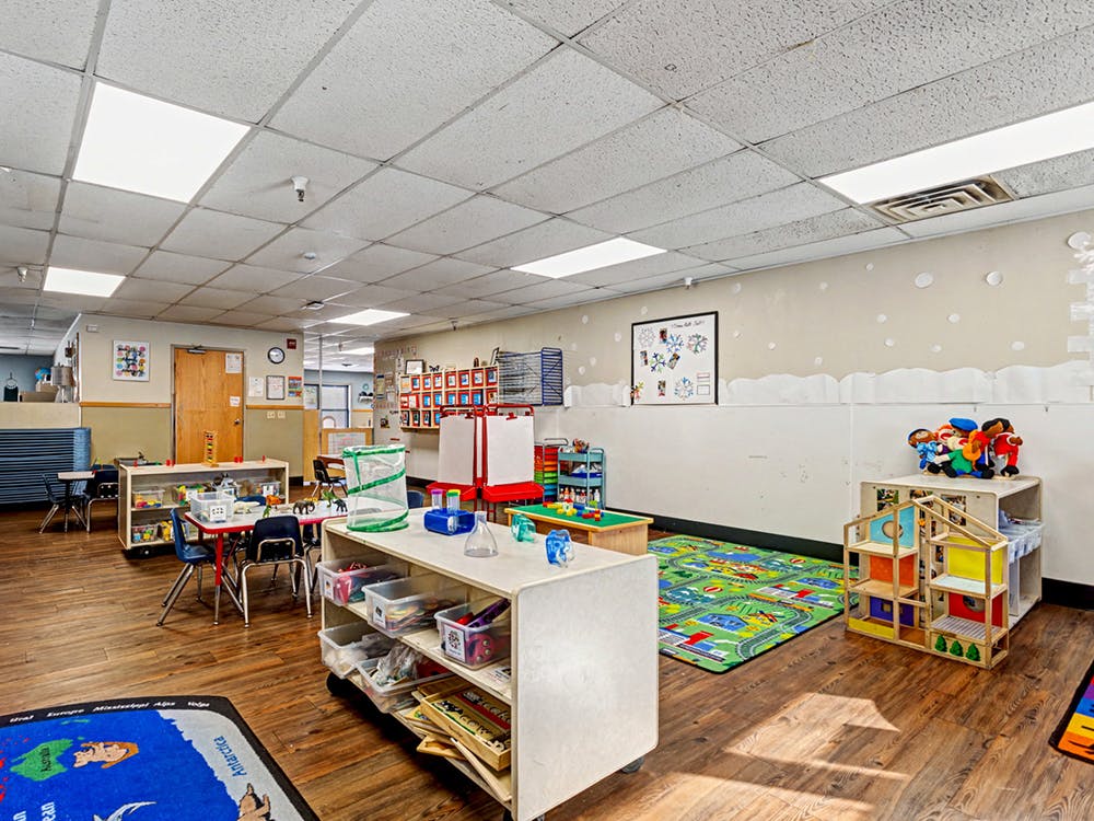 Classroom with tables, chairs, shelving units, and play mats
