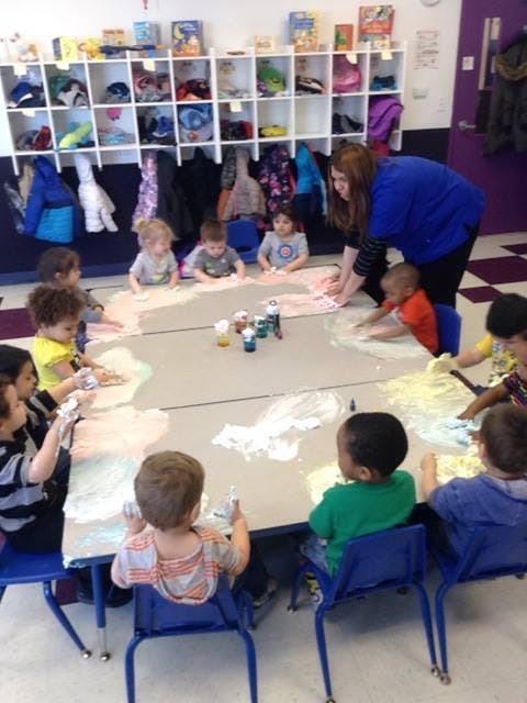 Adult and children doing an art activity at a table in a classroom