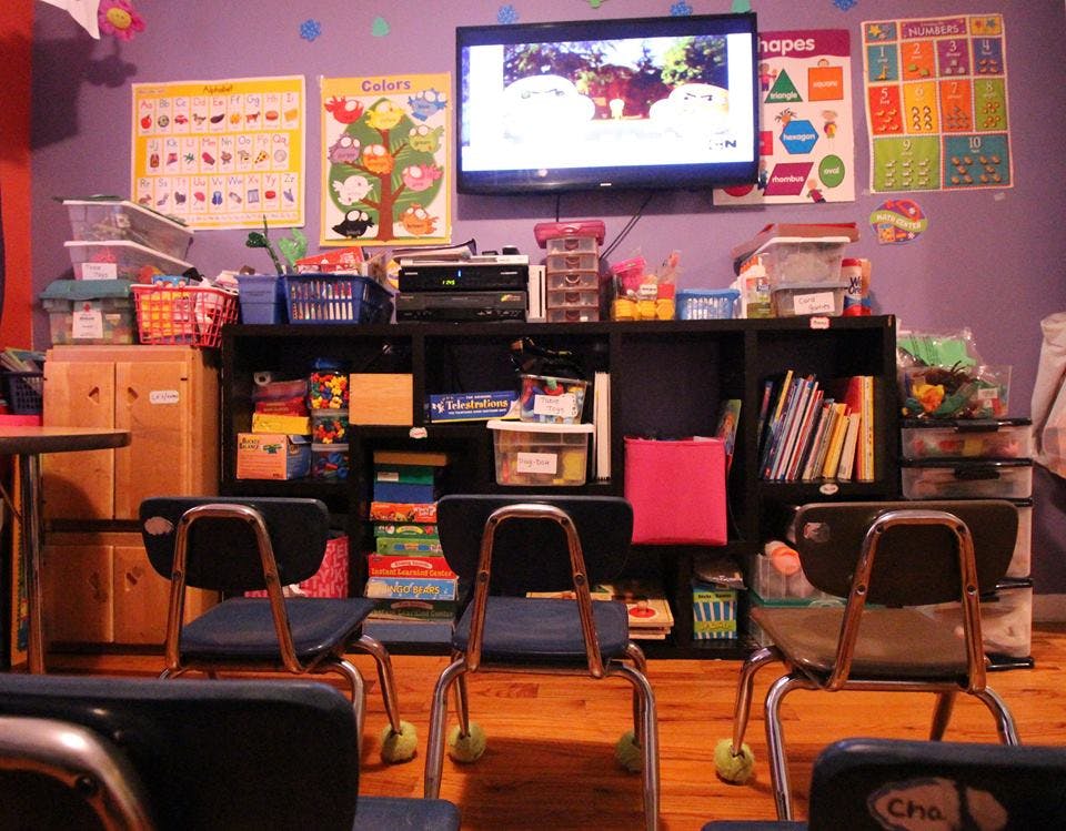 Classroom with chairs, shelves of supplies, and a TV screen