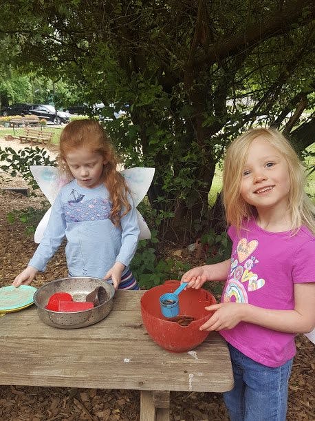 Two children playing with bowls and scoops on a wooden table outdoors