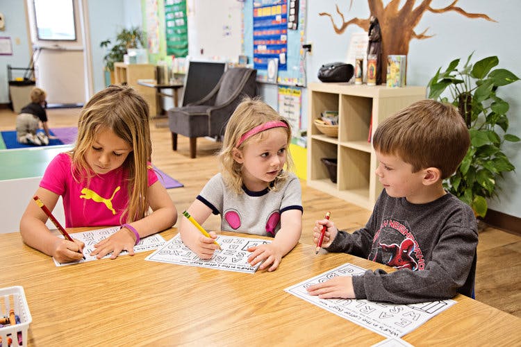 Three children coloring at a table in a classroom