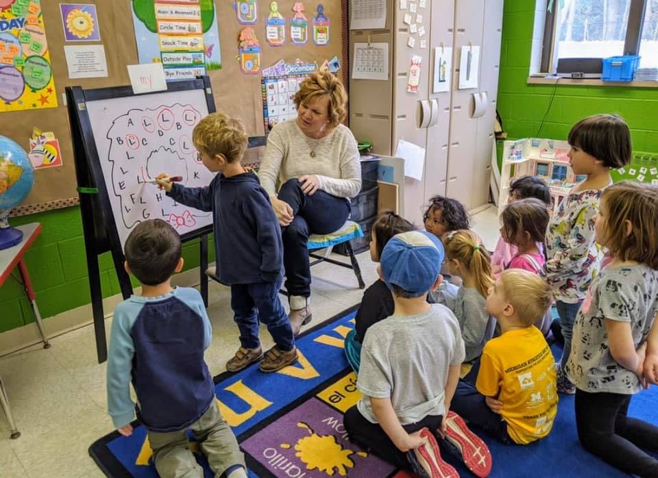 Adult and children in a classroom, child writing on an easel