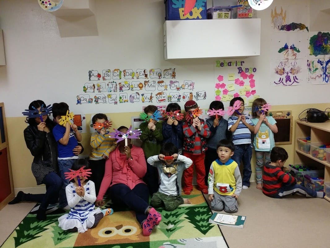 Group of children and adults holding masks to their faces in a classroom