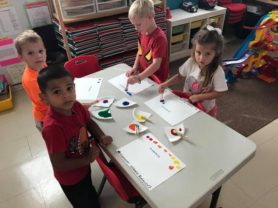 Three children painting at a table in a classroom