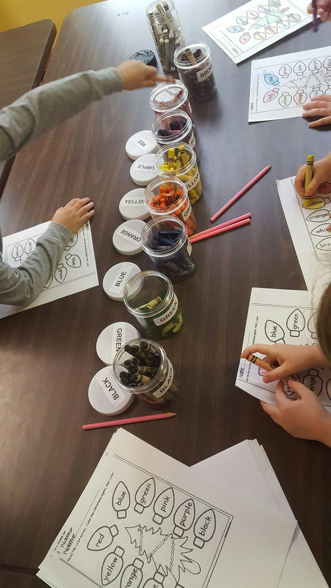 Children coloring at a table with jars of crayons