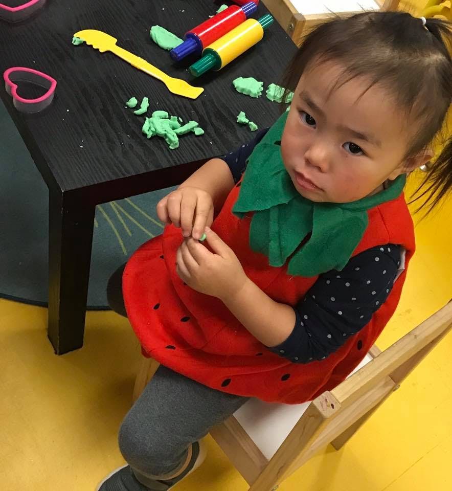 Child in a strawberry costume playing with modeling clay at a table