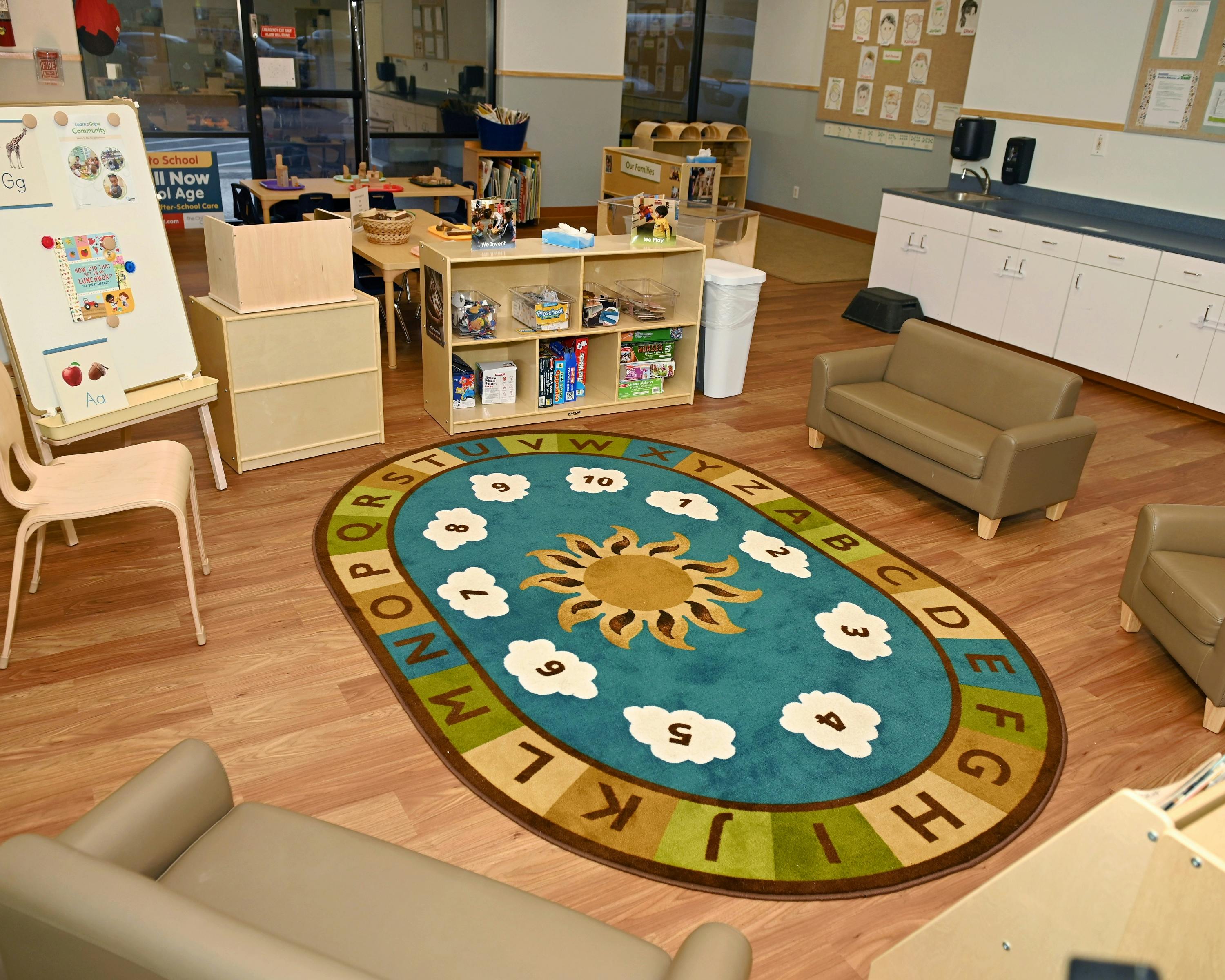 Classroom with a colorful ABC and number rug, easel, children's furniture, and shelves