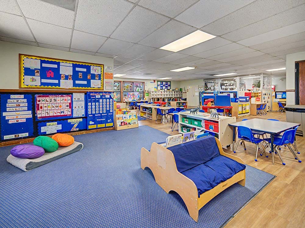 Colorful classroom with blue carpet, small tables, chairs, and learning materials