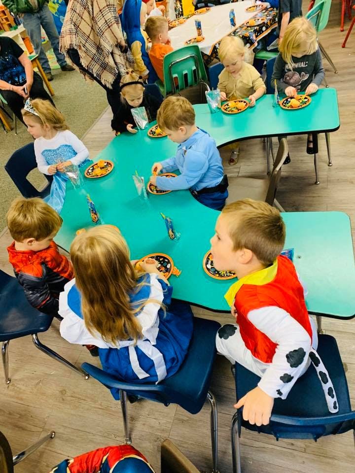 Children in costumes sitting at tables with plates