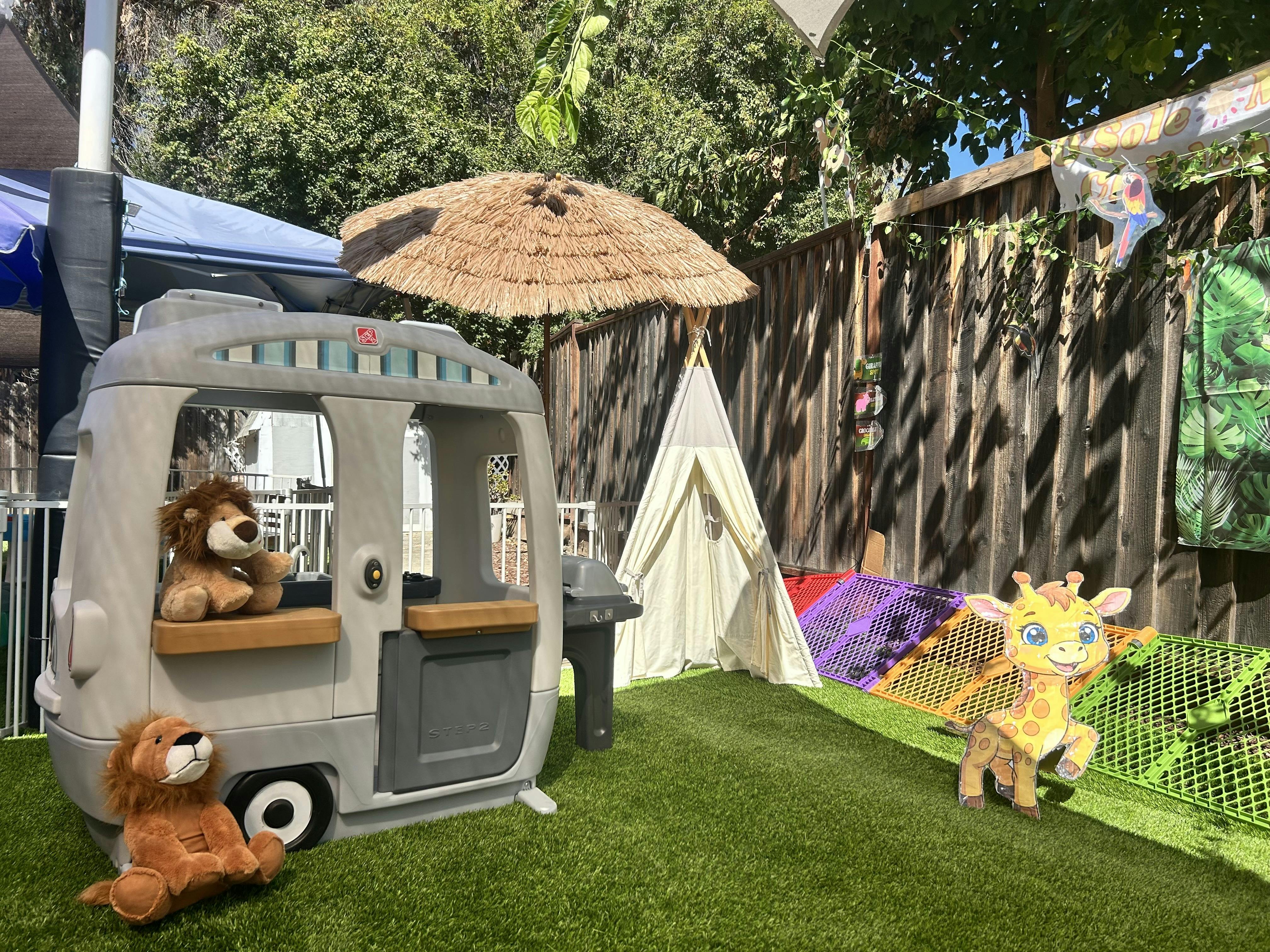 Play area with toy camper, small teepee, and plush lions on artificial grass
