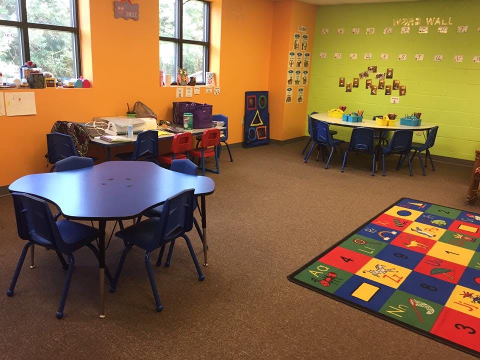 Classroom with small tables and chairs, and a colorful alphabet rug