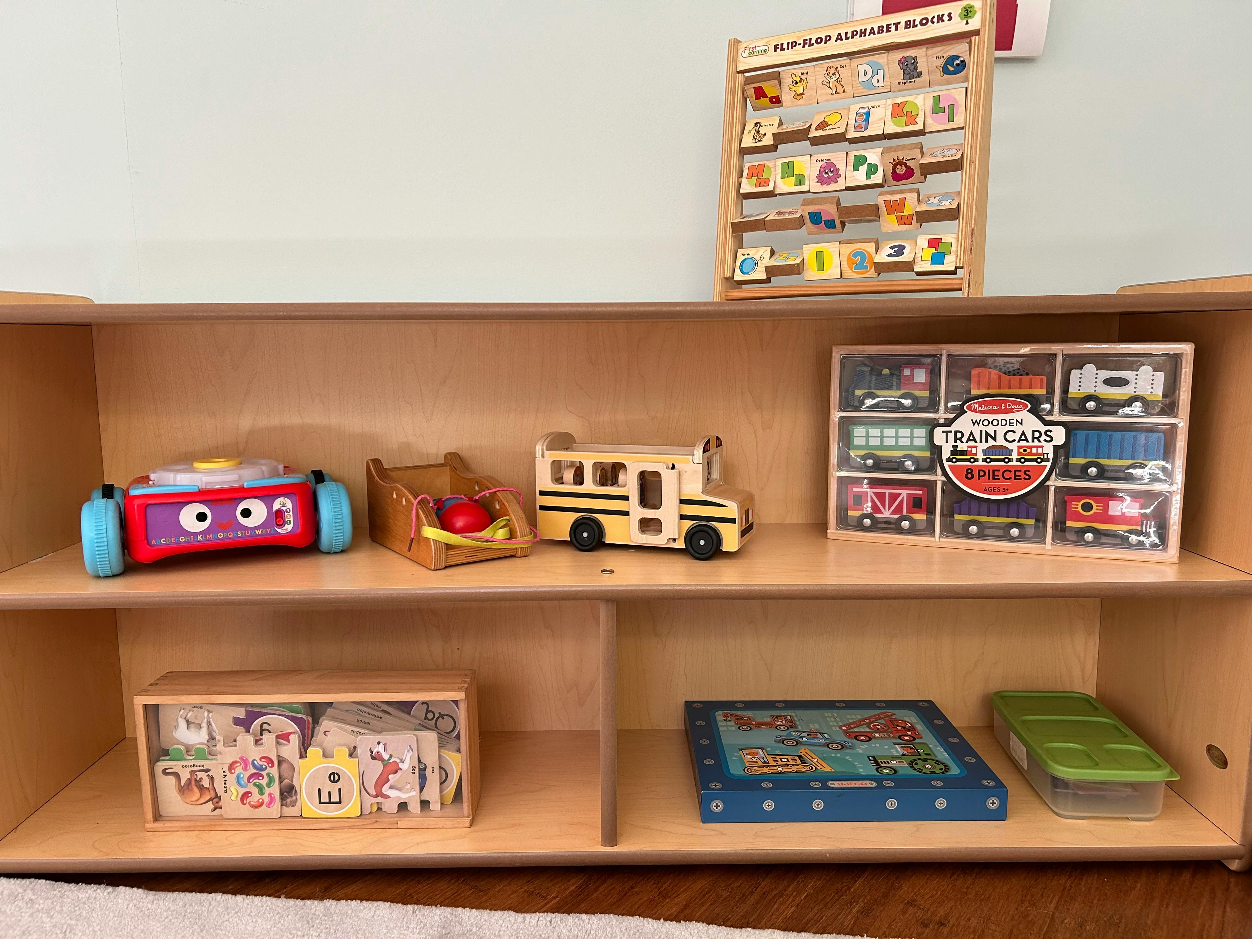 Wooden shelf with various toys including a school bus, train cars, and blocks