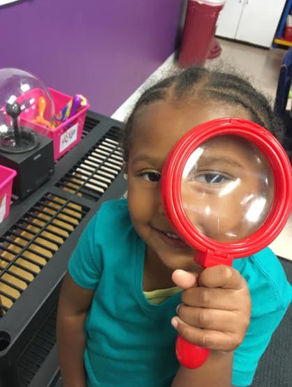 Child holding a red magnifying glass to their eye