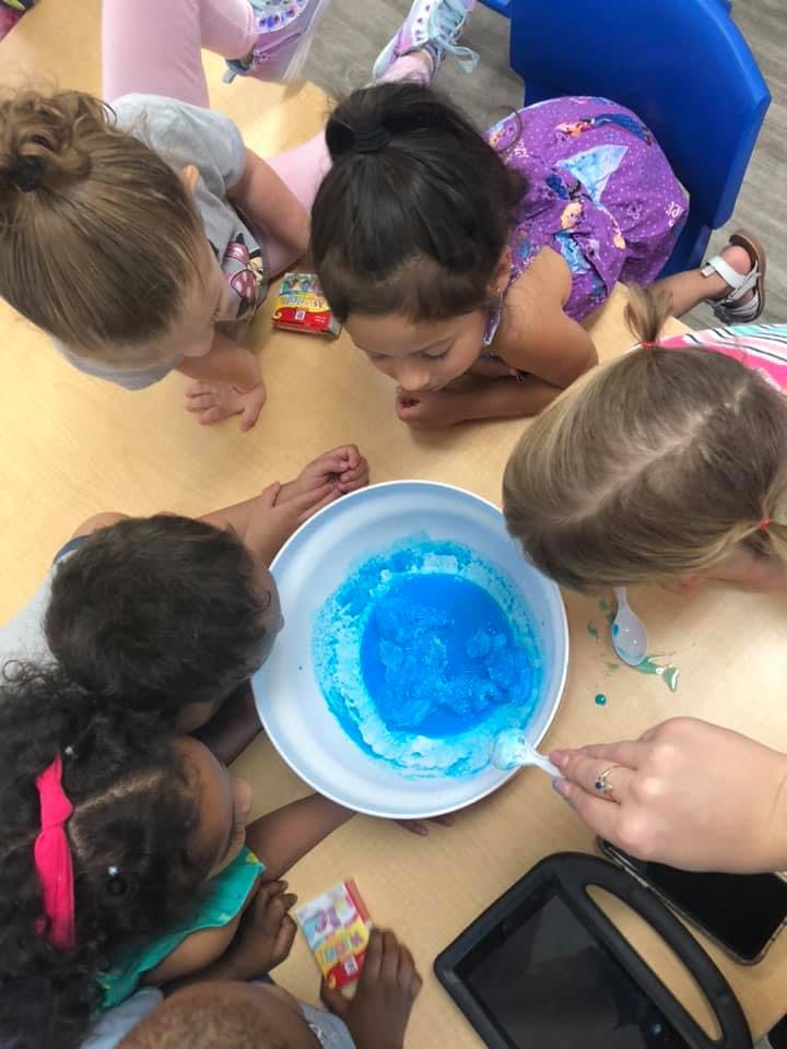 Children gathered around a bowl of blue liquid, one stirring with a spoon