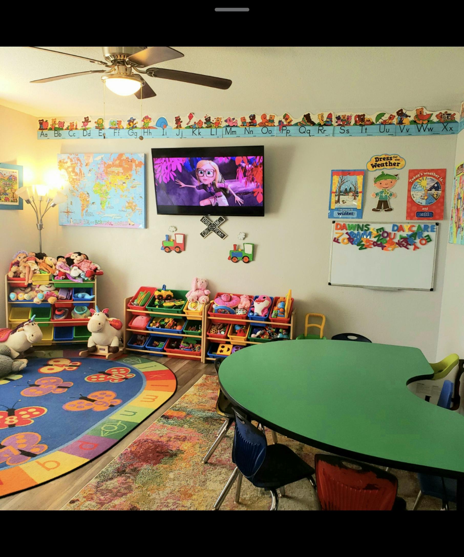 Classroom with a green table, colorful rug, and toy shelves