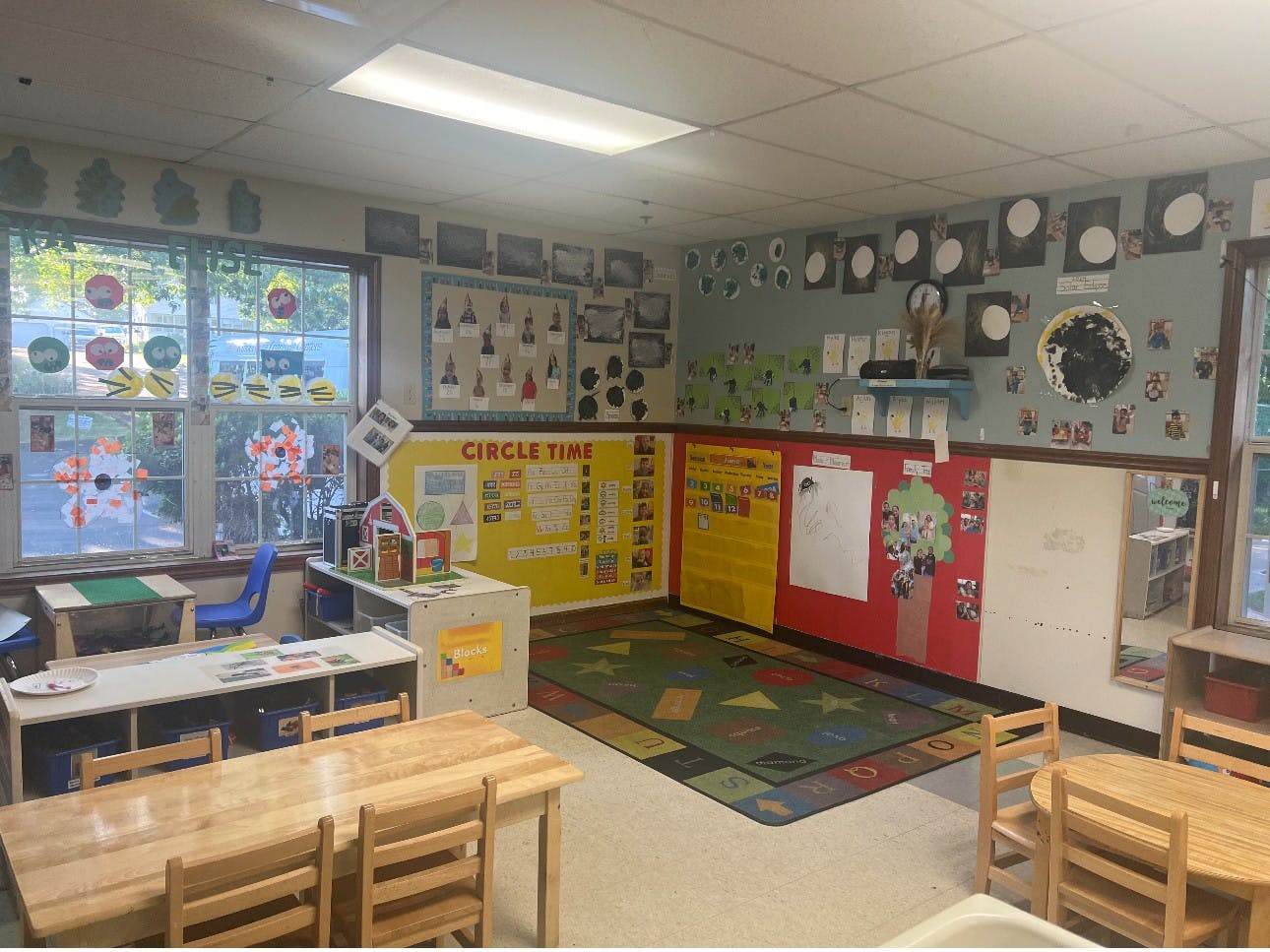 A colorful classroom with child-sized tables and chairs, a rug, and decorated walls