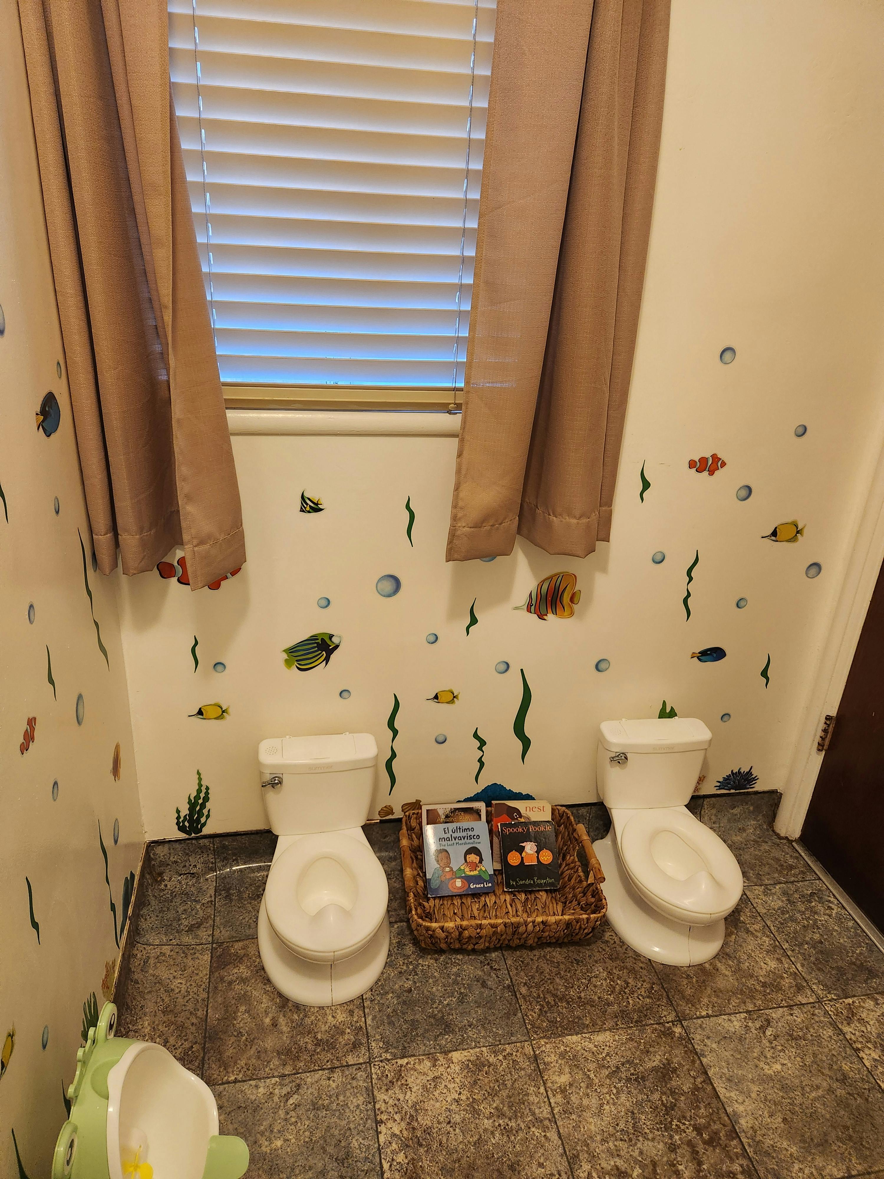 Two small toilets in a bathroom with fish wall decals