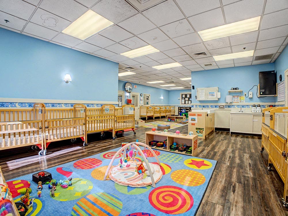 Baby room with multiple cribs, a colorful rug, and infant play mat