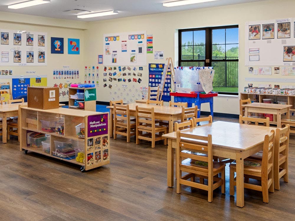 Empty classroom with small wooden tables and chairs, shelves, and a window