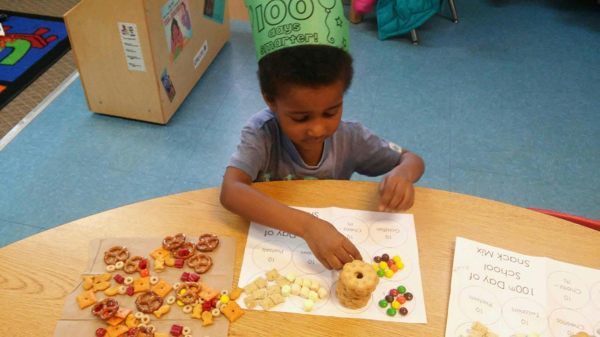 Child wearing a green crown making a snack on a paper in a classroom