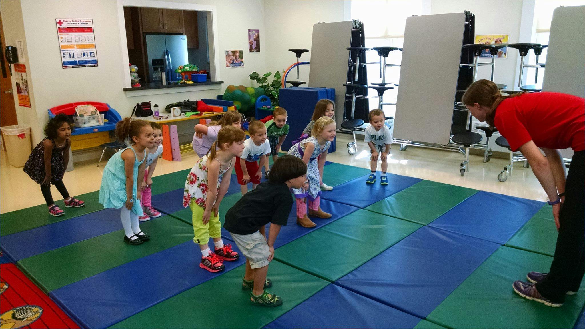 Adult and children bending over on a mat in a classroom