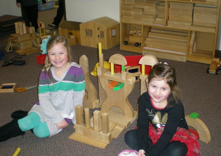 Two children sitting on the floor with wooden toys
