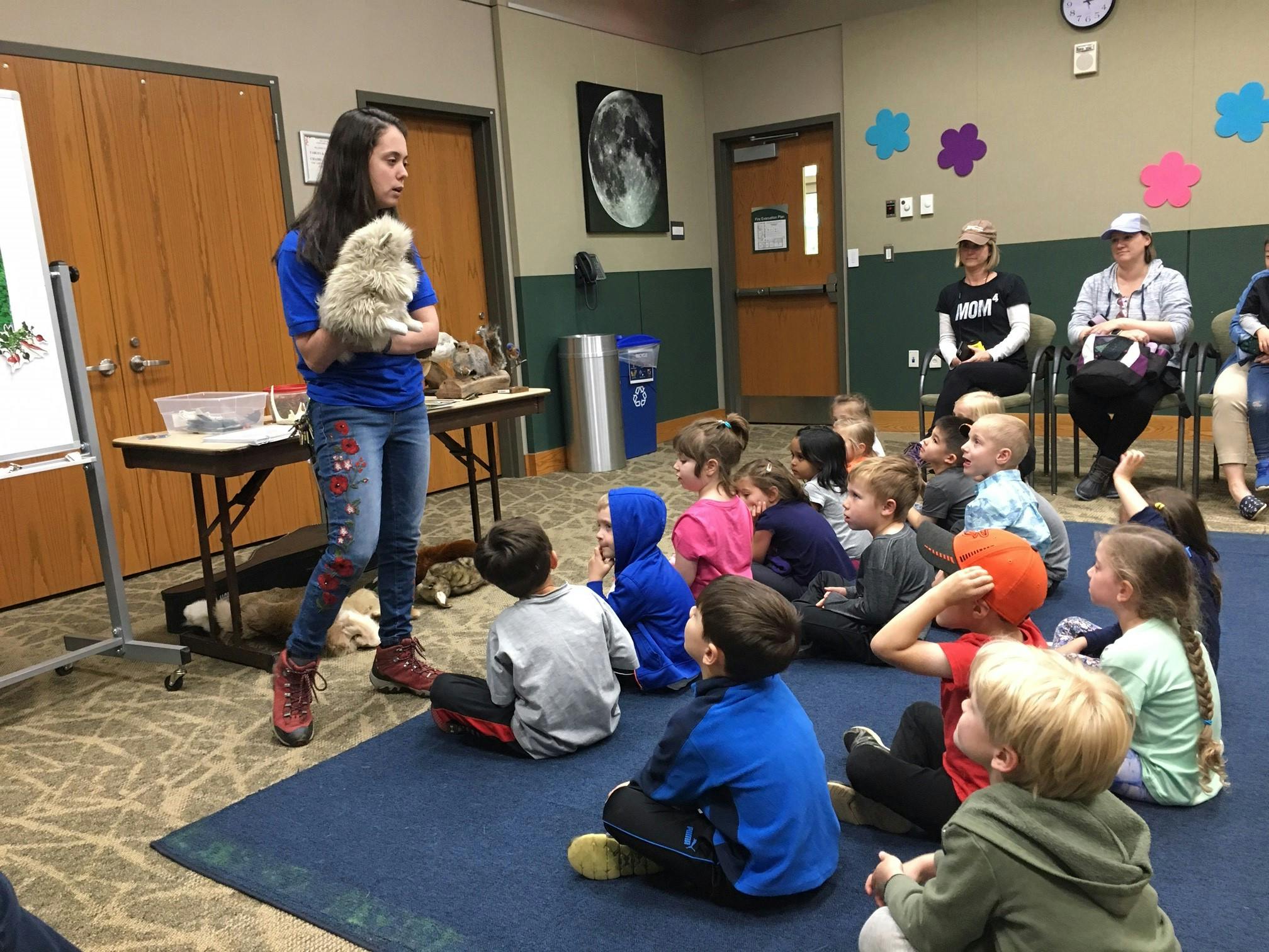 Person holding a small animal in front of seated children