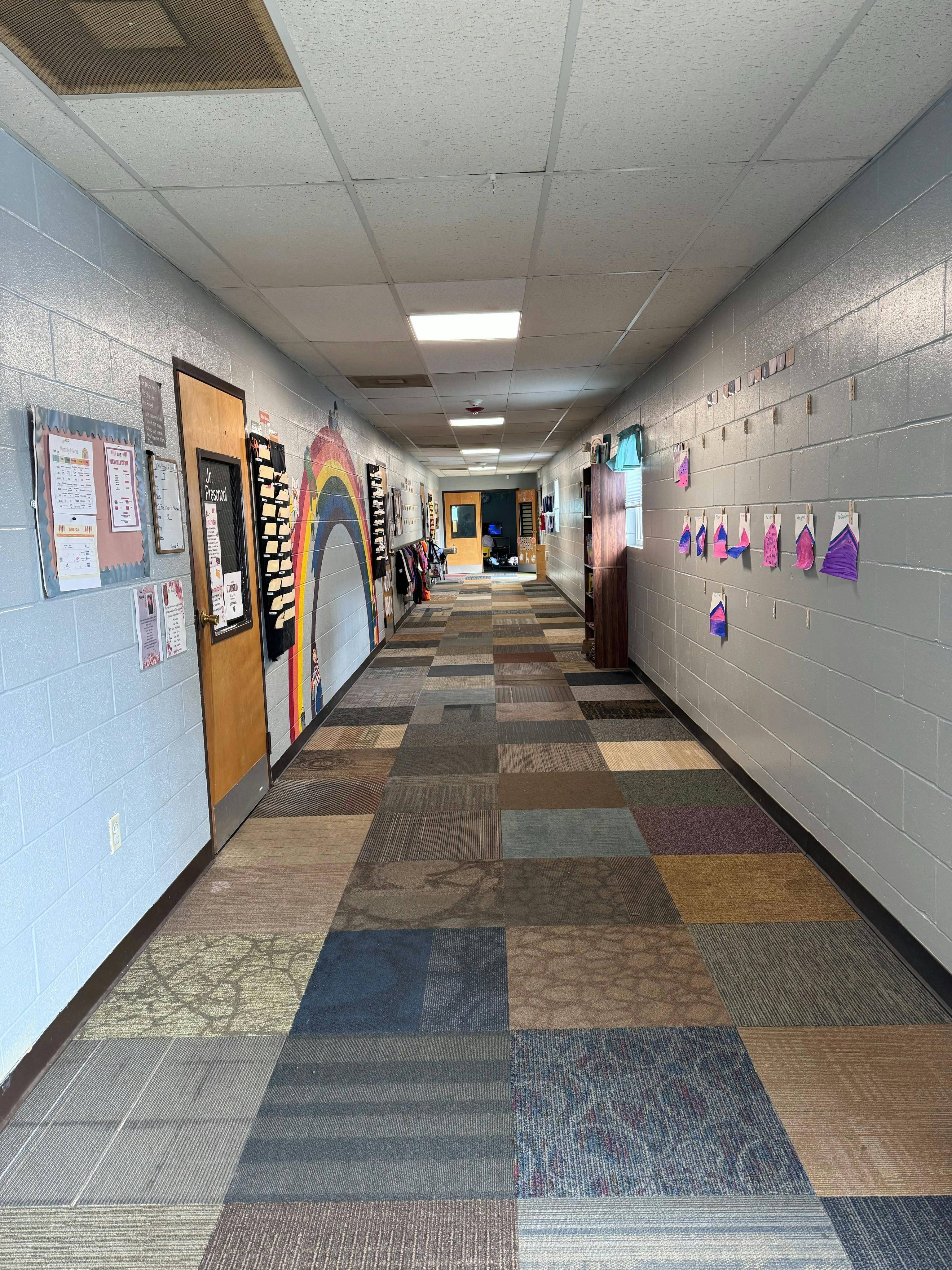 Long school hallway with decorated walls, patterned carpet, and open door to classroom