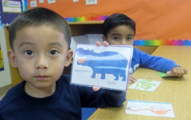 Child holding up a card with a blue hippopotamus illustration