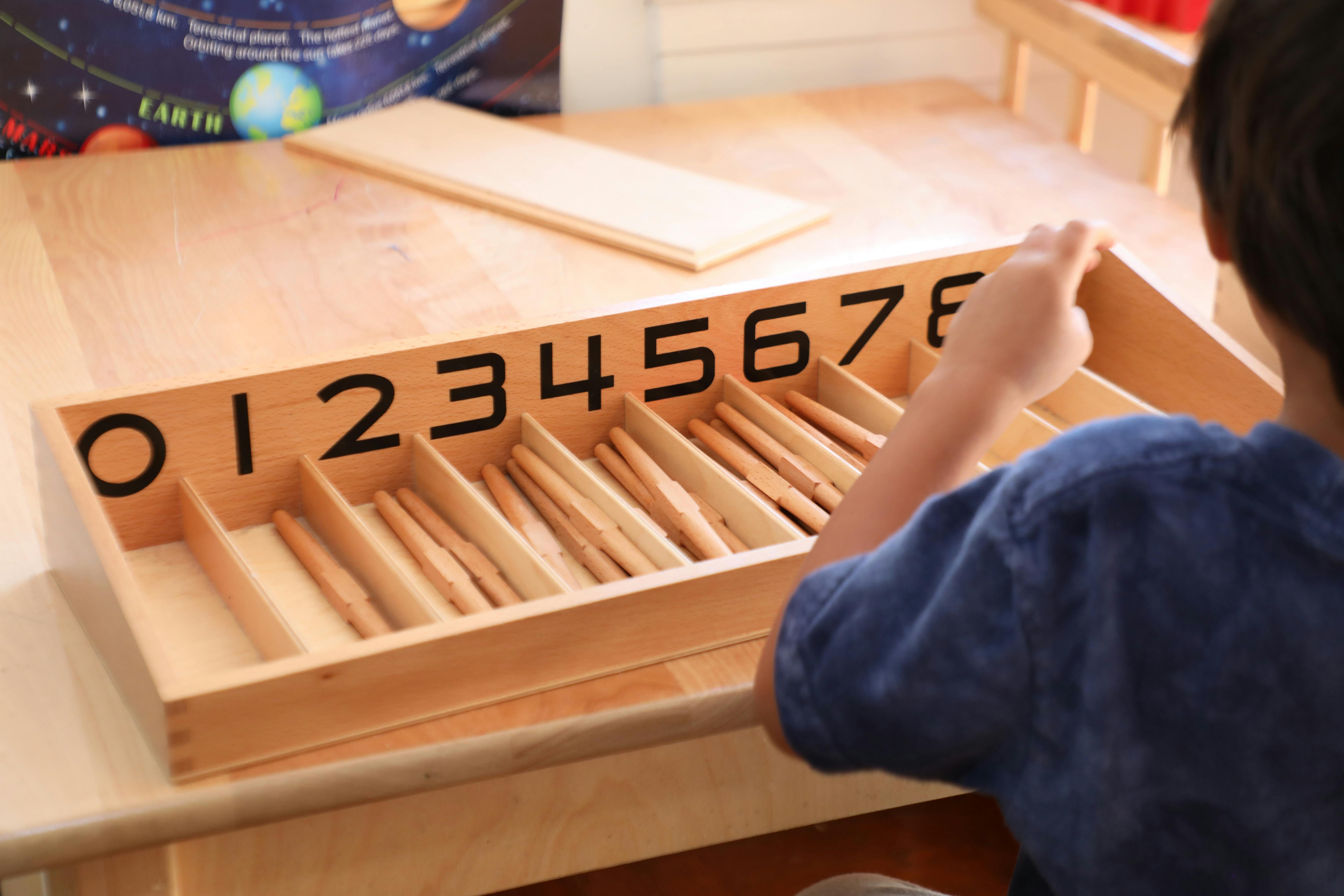 Child interacting with a wooden counting tray with numbers 0-7
