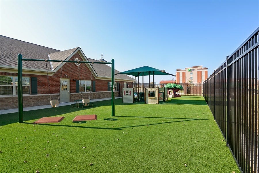Outdoor playground with swings, green turf, and a building in the background