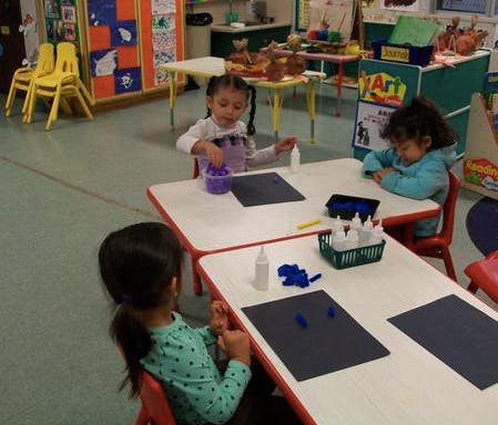 Three children at tables doing an art activity in a classroom