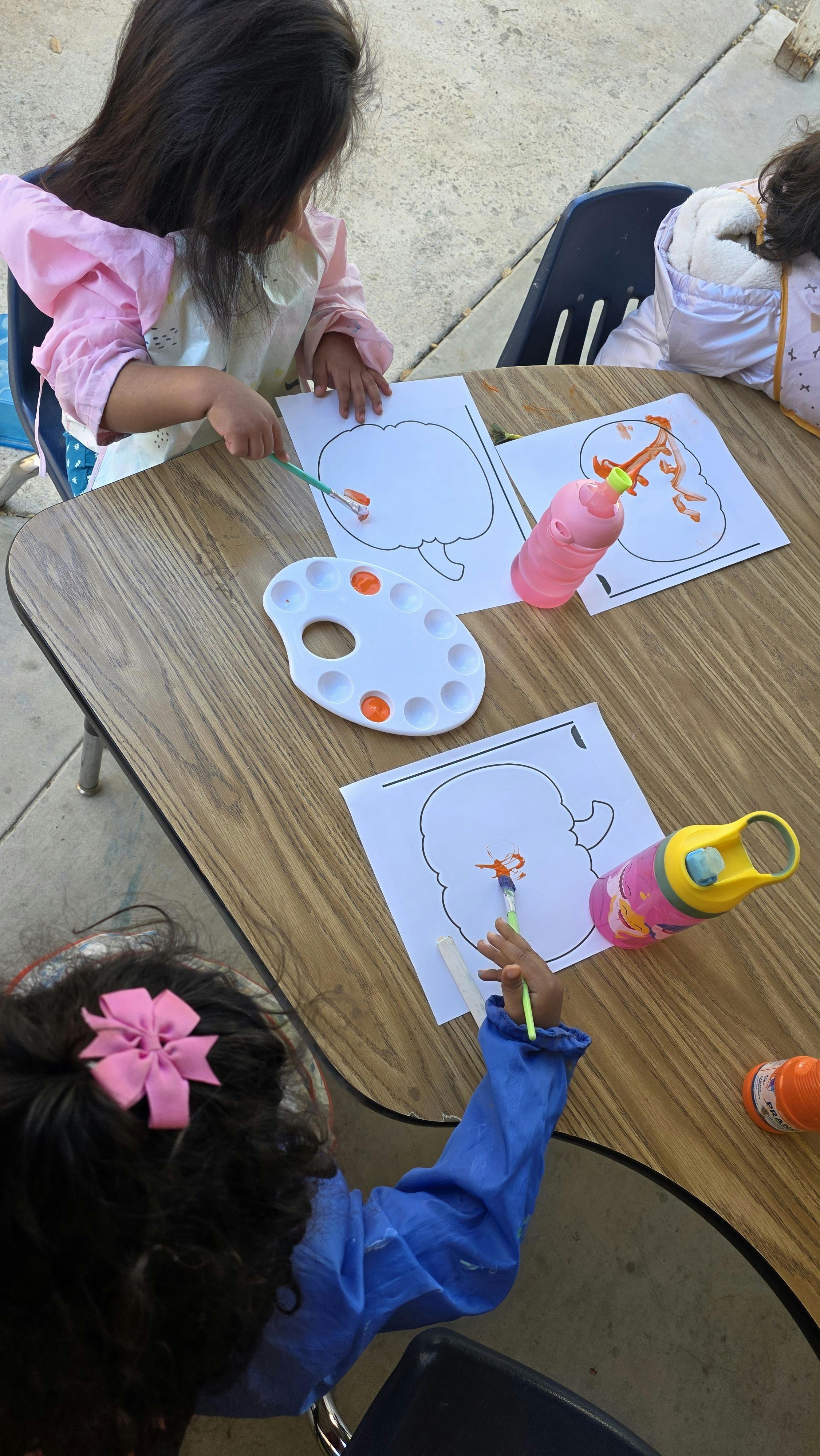 Children painting pumpkin outlines on paper at a table