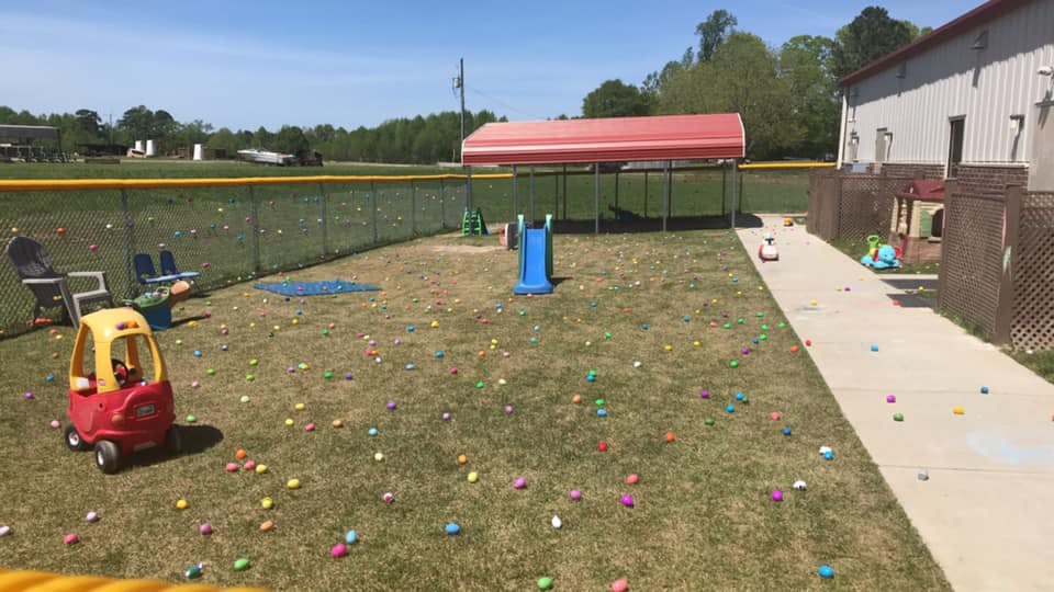 Outdoor play area with toy car, slide, and colorful eggs scattered on grass